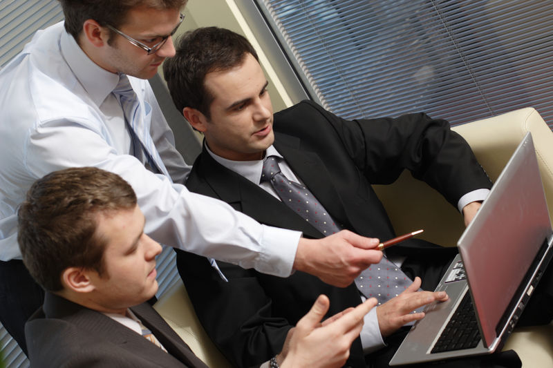 Business Owners and Asset Protection Jacksonville, Florida - a man with a laptop being handed a pen and talking with two colleagues